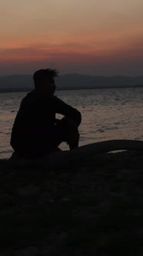 Vertikales Video der Silhouette eines Mannes am See bei Sonnenuntergang