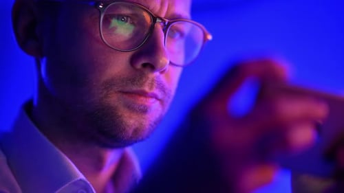 Caucasian Man in His 30s Wearing Glasses Browsing Data on His Smartphone