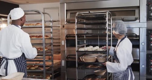 Happy diverse bakers in bakery kitchen preparing rolls in slow motion