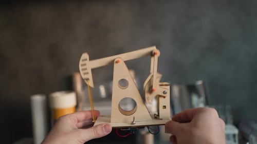 Hands Hold a Small Wooden Pumpjack Model