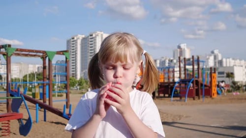 Little Cheerful Girl Portrait Inflates a Red Balloon on the Playground in Summer