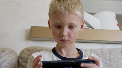 Blond Boy Playing on a Mobile Device Indoors
