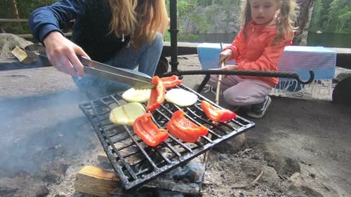 Young Mother and Daughter Grilling in the Forest on the Shore of the Lake