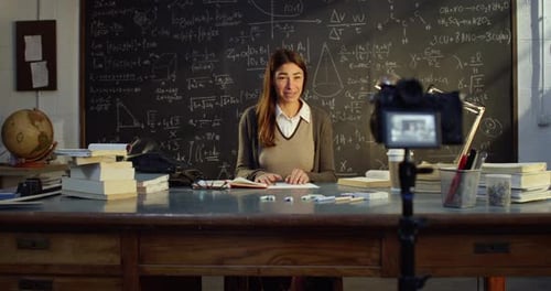 Woman Filming Educational Video at Desk with Chalkboard