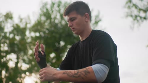 Man Wrapping Hands with Black Bandages Outdoors