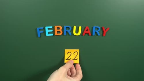 Hand sticking a sticker 22 February calendar day on school board. 22 date of February. Twenty