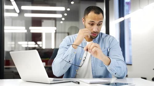 Man Taking Off Glasses at Office Desk