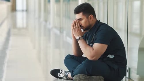 Concerned Doctor Seated in Hospital Corridor