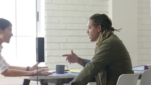 Two diverse designers in discussion at table in casual creative meeting, in slow motion