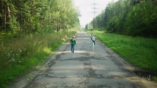 Young Siblings Walking On Tarred Road With Puddles In Forest