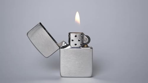 Un encendedor de metal gris se enciende sobre un fondo gris La llama del encendedor parpadea lentamente