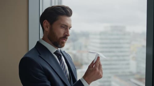 Bearded Businessman Holding Paper Airplane by Office Window