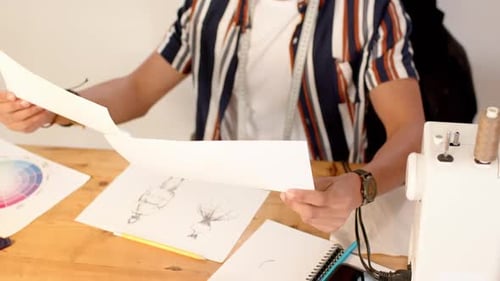 Biracial male fashion designer looking at sketched designs in studio, slow motion
