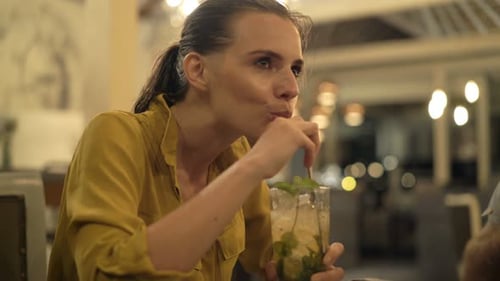Young, Happy Woman Drinking Mohito Sitting in Bar at Night 30s