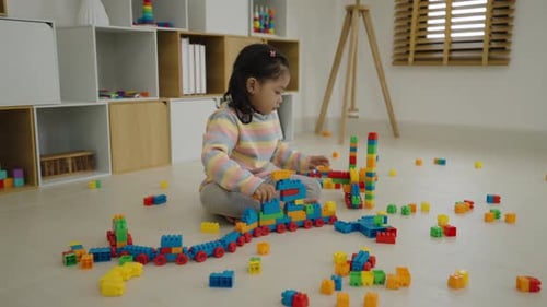 happy toddler girl playing building blocks or plastic bricks toy at home