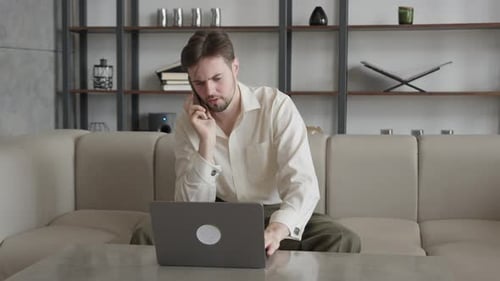 Young Creative Man with Laptop Talking on Smartphone in Office
