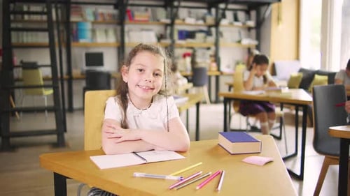 A Happy Elementary School Girl Sitting at a School Desk Looking at the Camera and Smiling