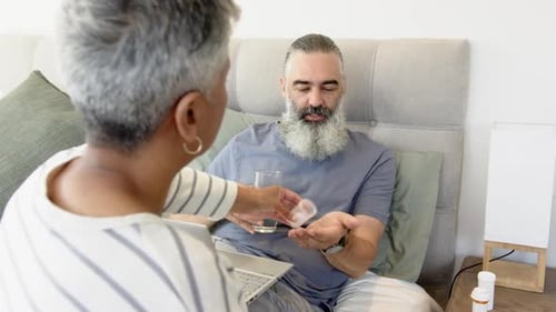 Woman Giving Medication To Senior Man In Bed