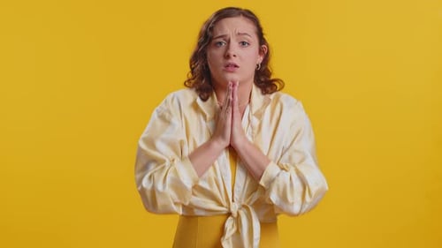Woman Pleading and Expressing Emotions Against Yellow Backdrop