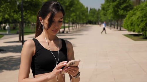 Closeup of a Young Woman with a Phone and a Smartwatch Before Jogging in a Park