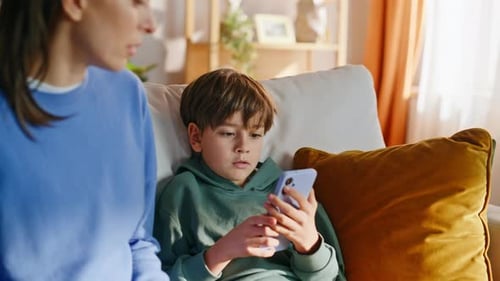 Boy Using Phone While Woman Talks on Couch
