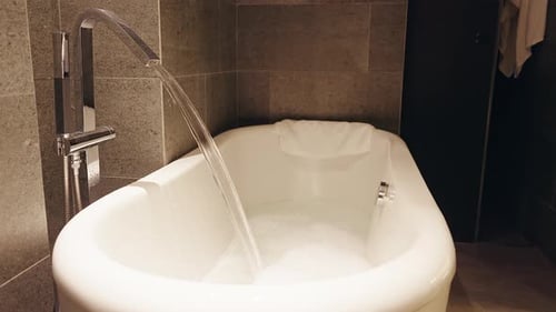 Wide Angle Bathroom View of Bathtub Filling with Foam Under Steady Water Stream Creating Cozy