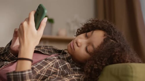 Teenage Girl Lies Relaxed Using Mobile Phone on Couch
