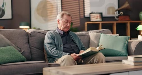 Senior Man Reading Book on Couch at Home