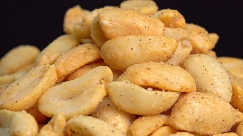 Roasted peanuts rotate on black background, peanuts without shells, ground nuts. Spiced peanuts