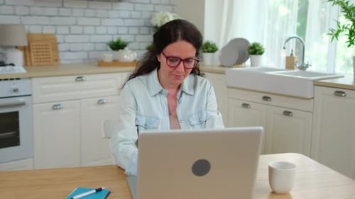 Woman Uses Laptop at Kitchen Table Indoors Daytime