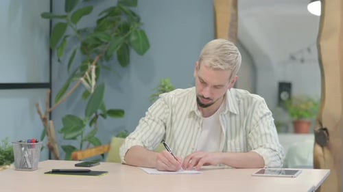Modern Young Man Writing while Sitting in Office