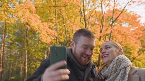 Smiling Couple with Dog Taking and Watching Selfies on Smartphone in Fall Park