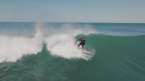 Male surfer riding the big ocean wave on a sunny day by the coastline