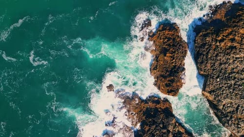 Turquoise sea waves splashing at seashore cliffs in super slow motion aerial view