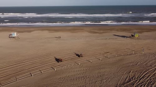 Two Friends driving quad vehicle along sandy coastline of Argentina during sunset - Aerial tracking