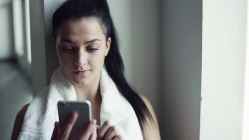 Young Woman with Smartphone in Gym Resting After Doing Exercise