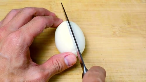 Person Cuts Hard Boiled Egg on Board