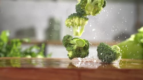 Slow motion of fresh green broccoli slices falling on wet wooden board in a kitchen