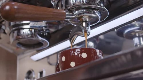 Idyllic slow-motion close-up of an industrial coffee maker pouring fresh coffee in a cup to keep up