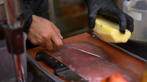 Hand in Black Gloves Cutting Pineapple on a Chopping Board at Street