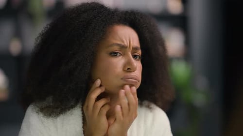 African American Girl Woman Female in Bathrobe in Morning Looking in Mirror Touching Unhealthy Face