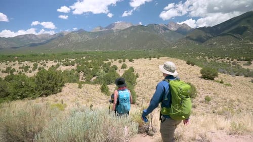 Hikers walking on dirt trail through the desert with rocky mountains in the background, static