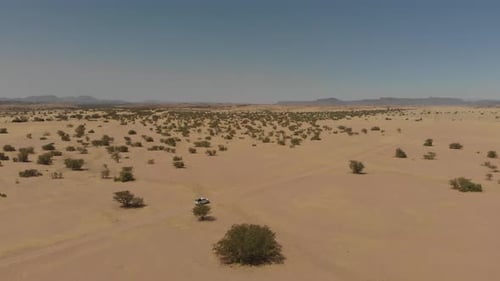 Distant aerial follow shot of vehicle driving alone through desert.