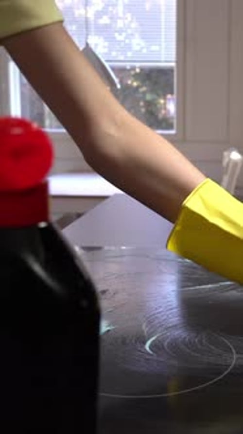 Person Cleaning Cooktop With Sponge and Gloves