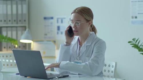 Female Doctor Talking on Phone While Using Laptop
