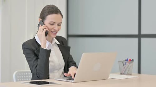 Woman Works on Laptop and Talks on Phone