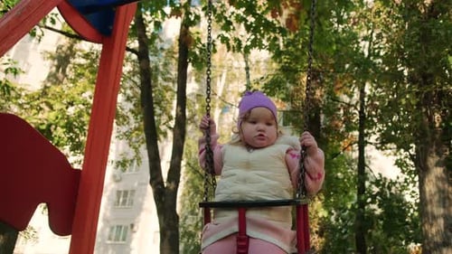 A Joyful Toddler Swings in the Park Wearing a Purple Hat and a Cozy Vest Bright Autumn Leaves Create