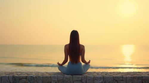 Femme mince pratiquant le yoga en méditant en position zen près de l'océan lors d'un coucher de soleil doré.