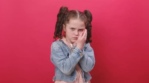 Little girl touching cheek, closing eyes with expression of terrible suffer from painful toothache