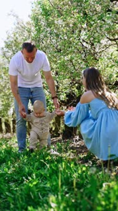 Smiling Caucasian man leading his infant baby by the hands in the garden.